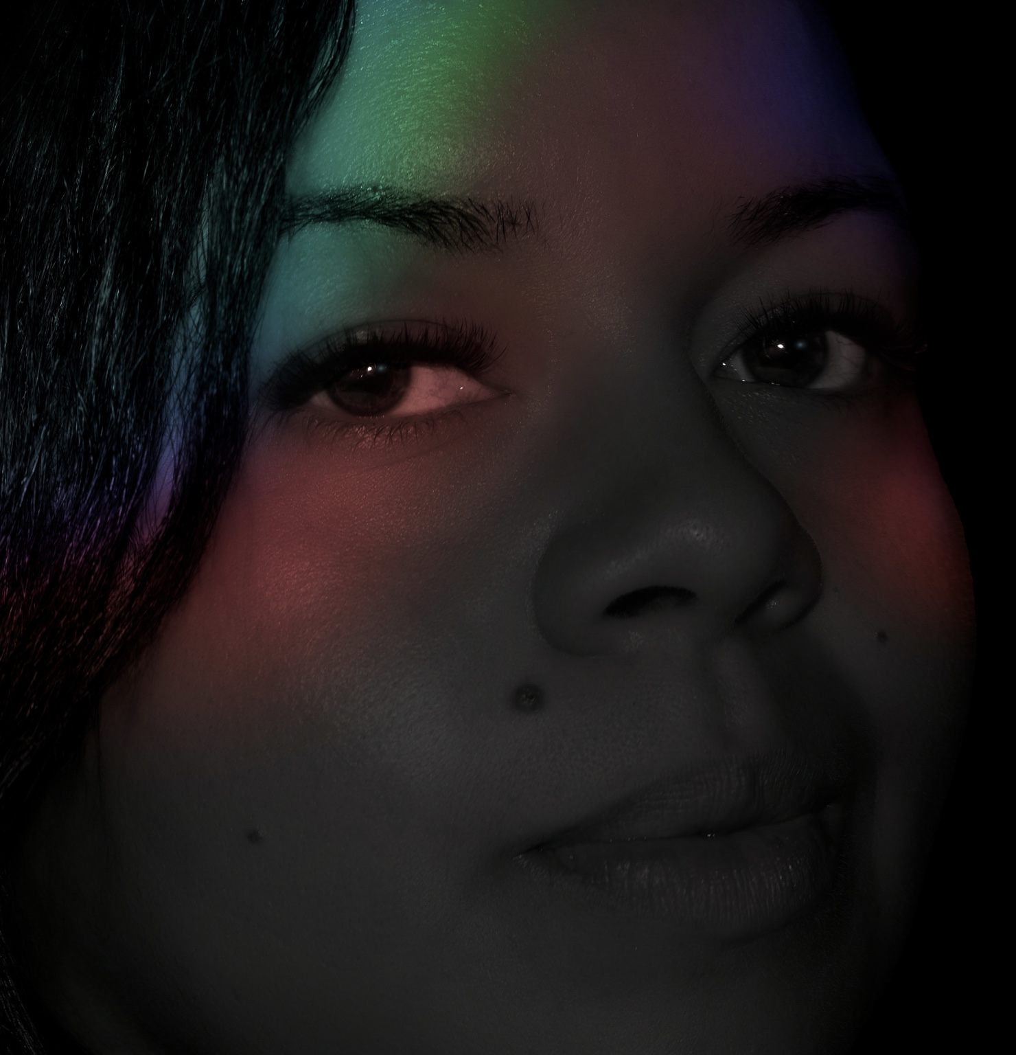 Primer plano de una mujer con reflejos verdes, violetas y rojos sobre el rostro.