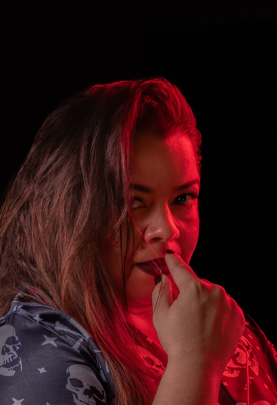 Retrato de una mujer con una mano junto a los labios y luz roja sobre el cabello y el rostro.