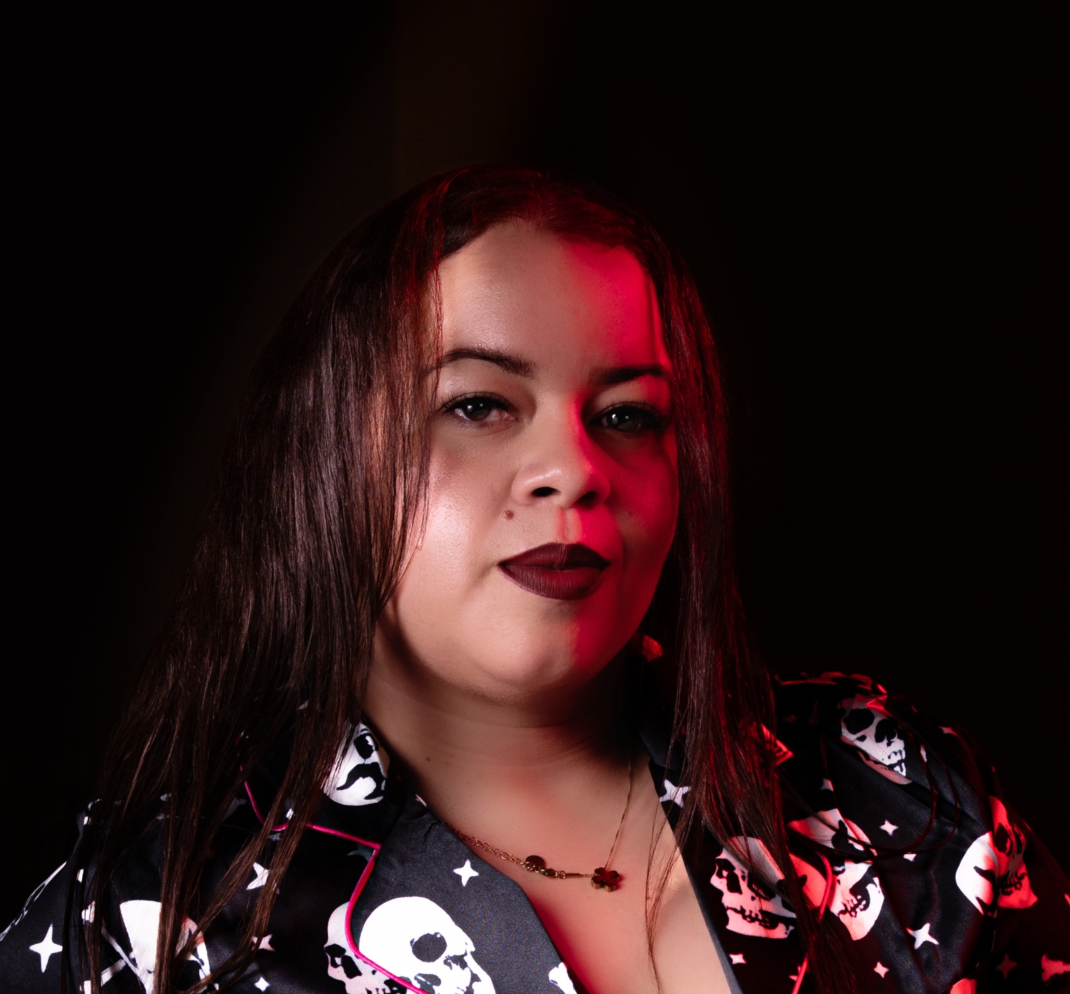 Retrato frontal de una mujer con luz roja lateral y camisa estampada.