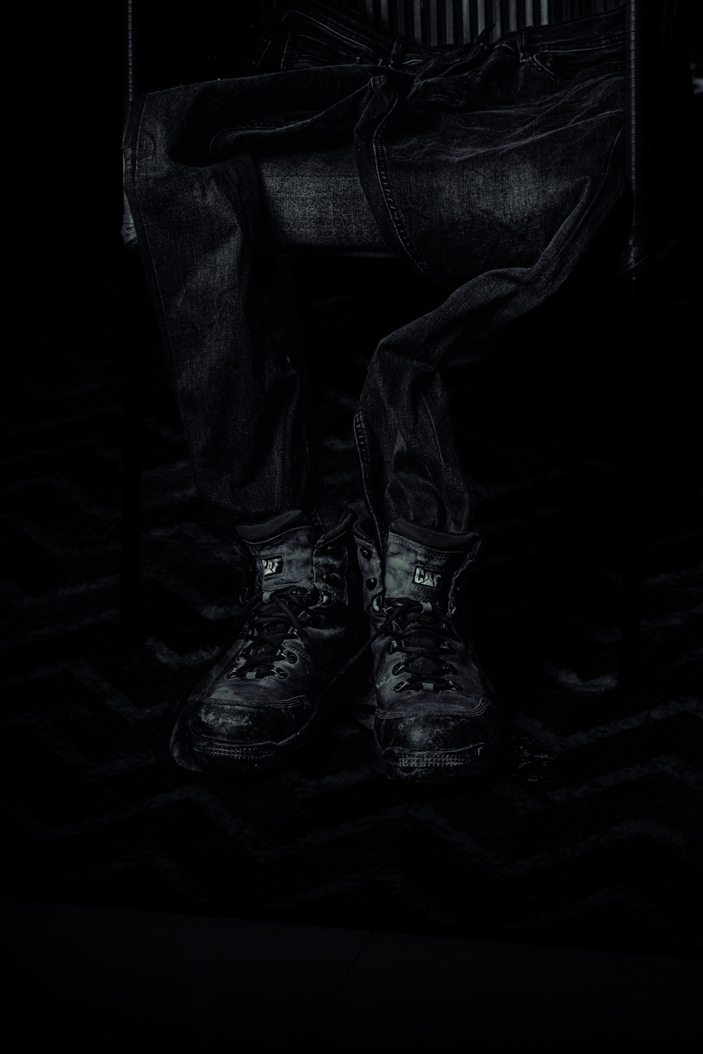 Un pantalón vaquero sobre una silla y unas botas gastadas emergen de las sombras.