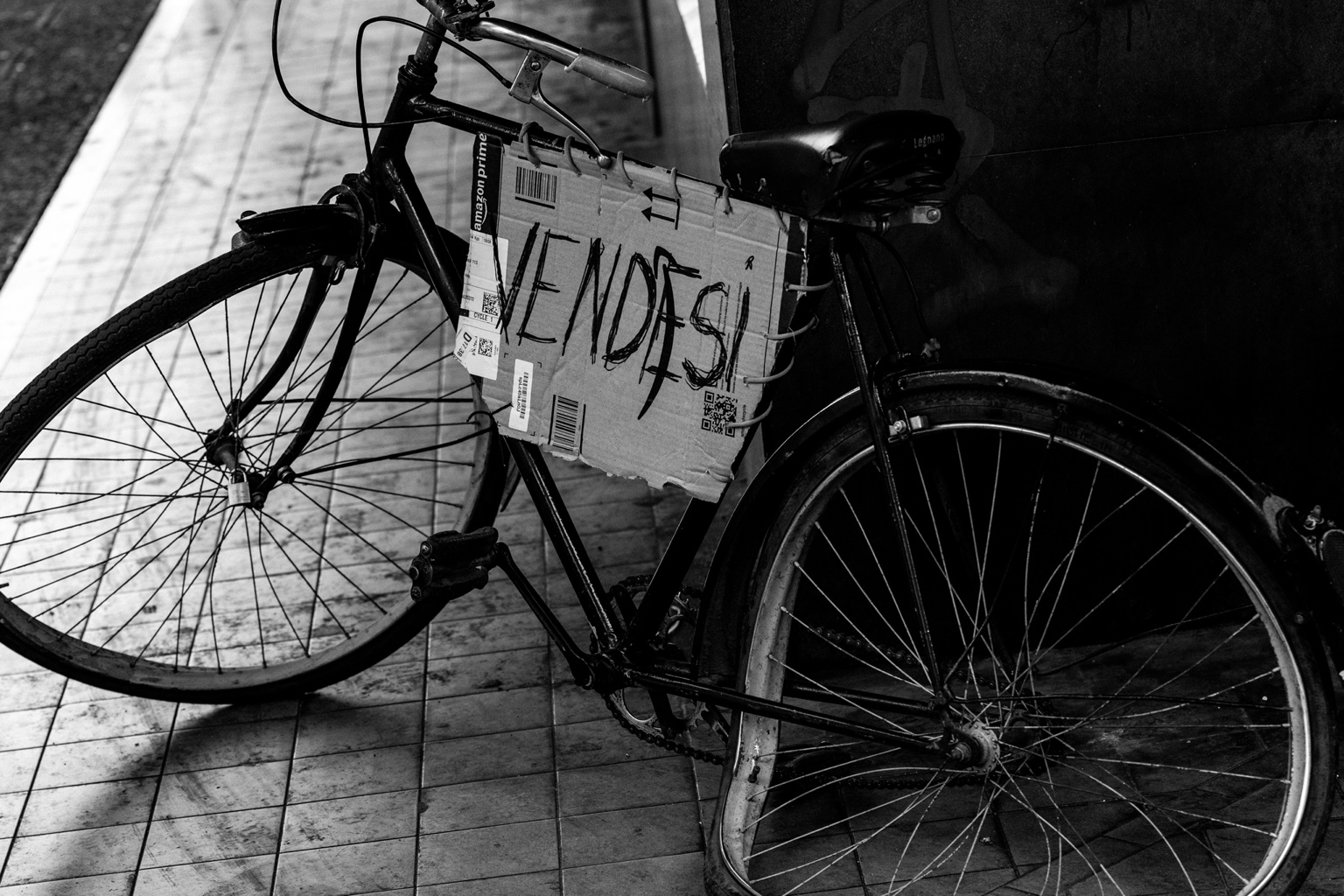 Una bicicleta apoyada en una pared con un cartel de venta.