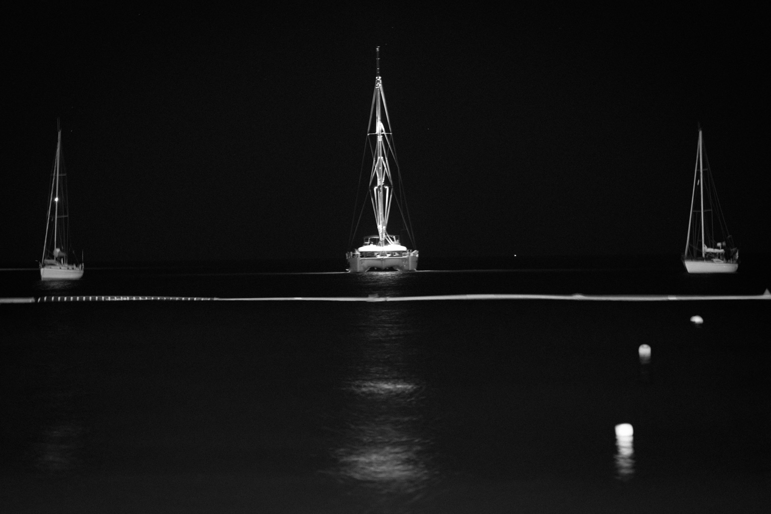 Tres veleros anclados de noche, con reflejos sobre el agua oscura.