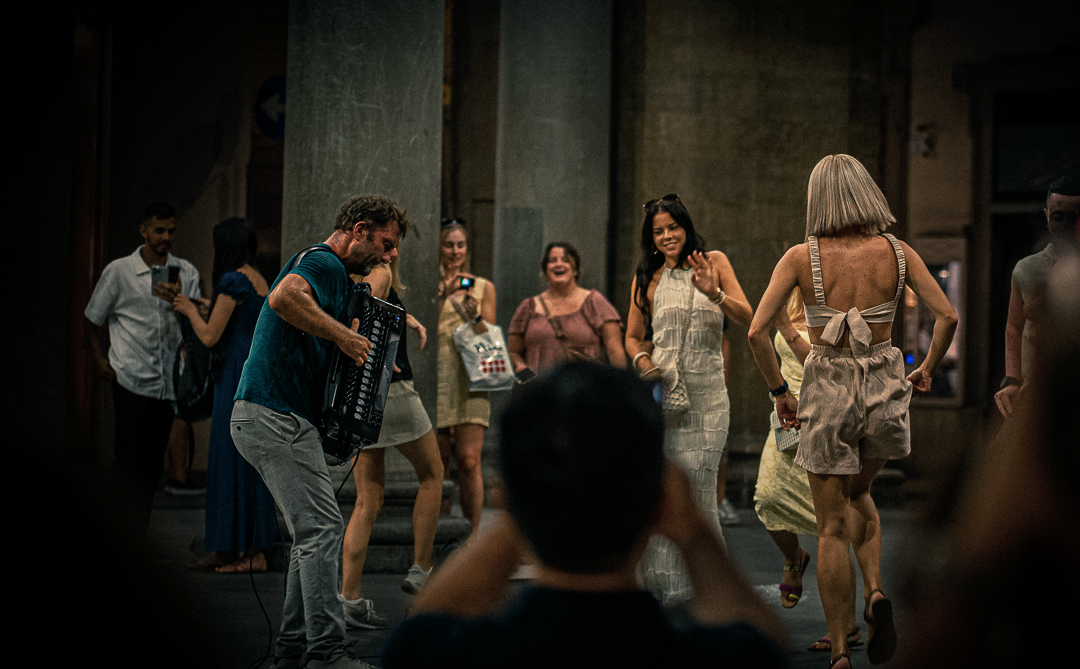 Un acordeonista toca entre personas que bailan y observan en la calle.