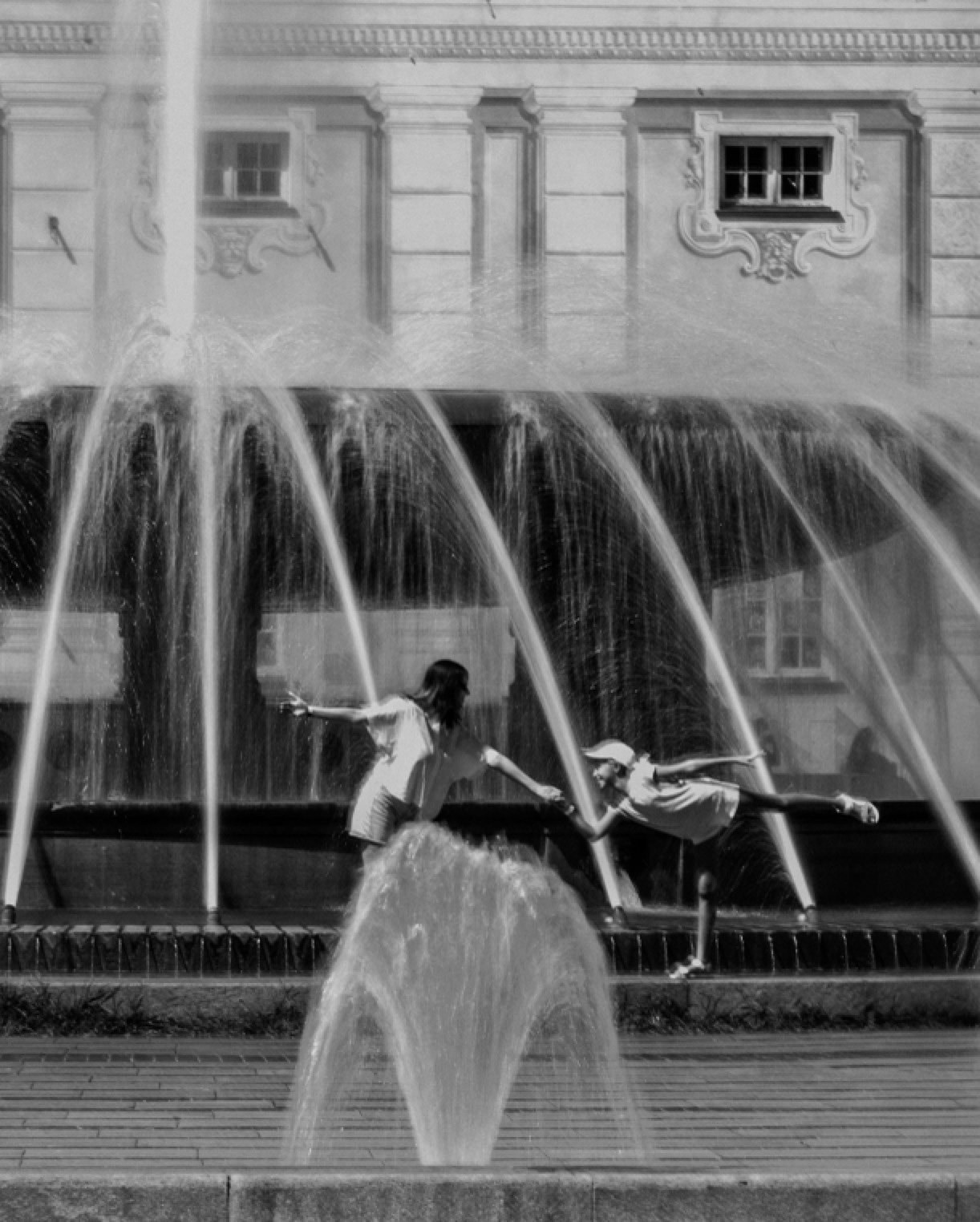 Personas jugando entre los chorros de una fuente, en blanco y negro.