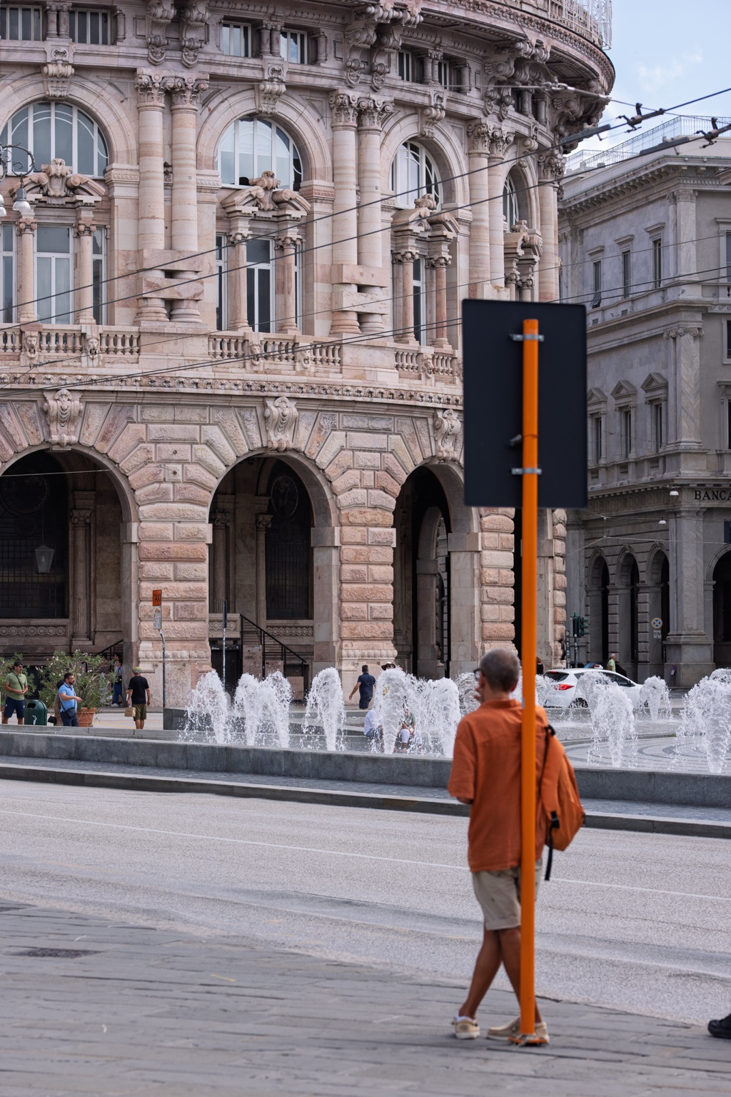Un hombre vestido de naranja pasa junto a un poste naranja frente a una fuente.