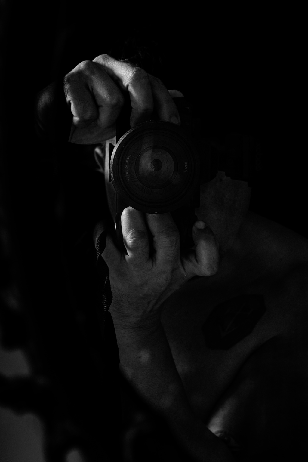 Autorretrato vertical en blanco y negro, con las manos alrededor de una cámara.