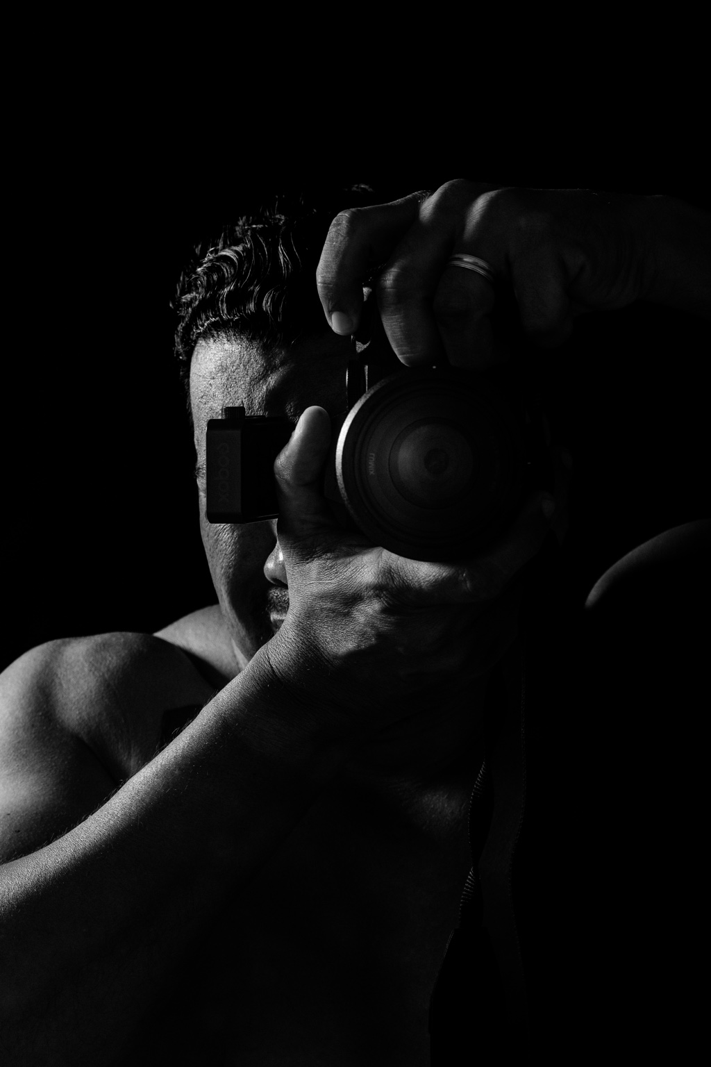 Autorretrato en blanco y negro con una cámara frente al rostro e iluminación lateral.