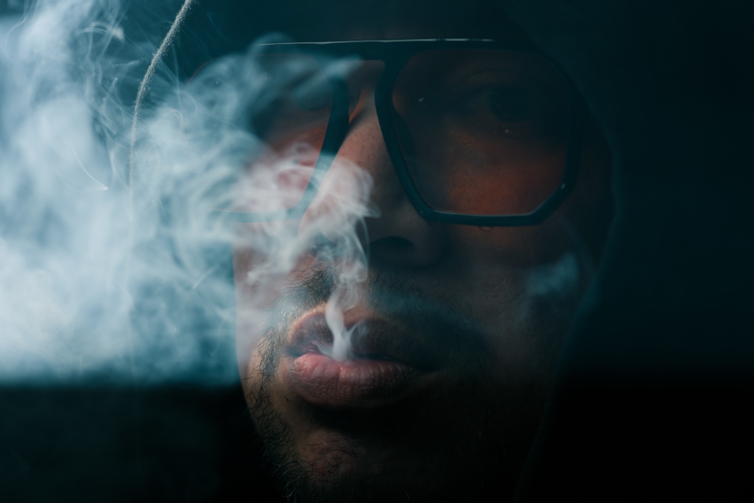 Retrato con capucha, gafas ámbar y una columna de humo iluminado.