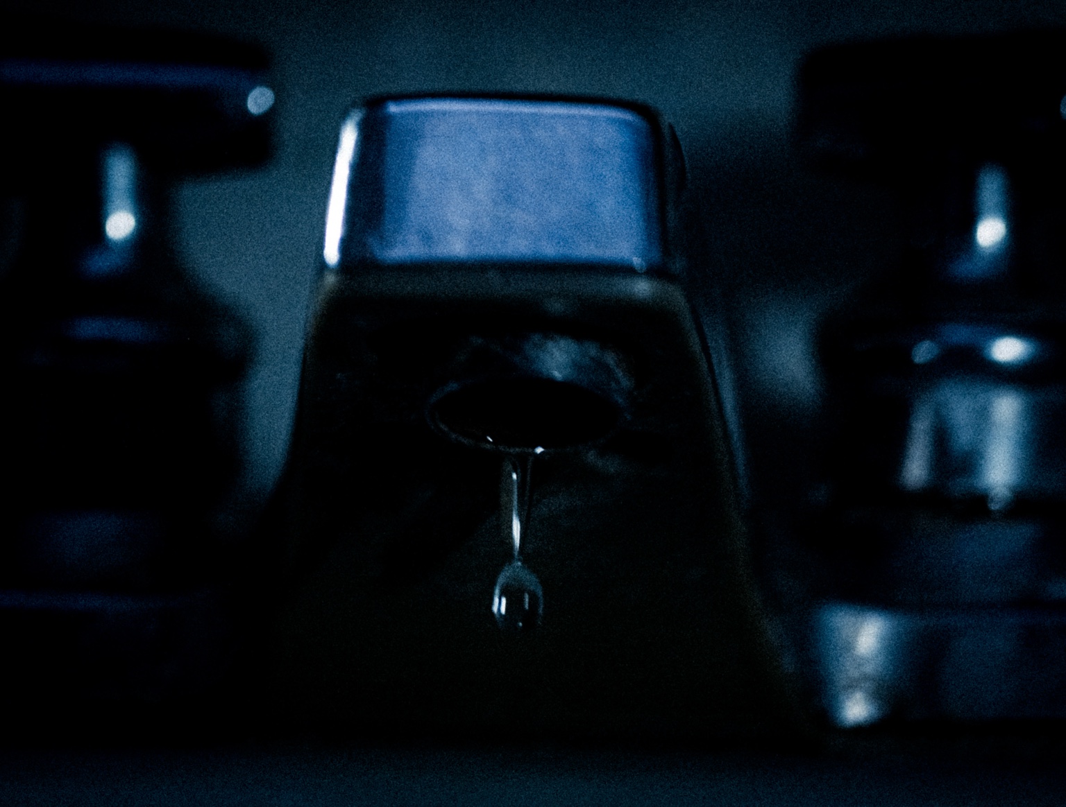 Primer plano de un grifo con una gota suspendida bajo luz azul.