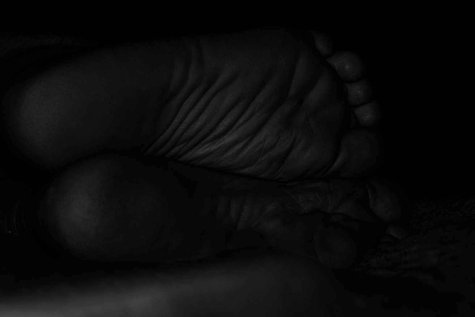 Detalle en blanco y negro de las plantas de unos pies, con sombras profundas.