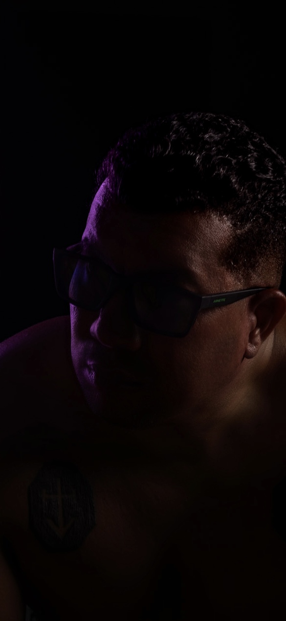 Retrato vertical con gafas oscuras y luz violeta lateral sobre el rostro.